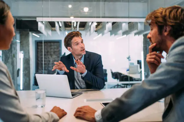 Shot of a young couple having a consultation with a financial advisor in the office. Group of business persons in business meeting. Three entrepreneurs on meeting in board room. Corporate business team on meeting in modern office. Male manager discussing new project with his colleagues. Company owner on a meeting with two of his employees in his office.